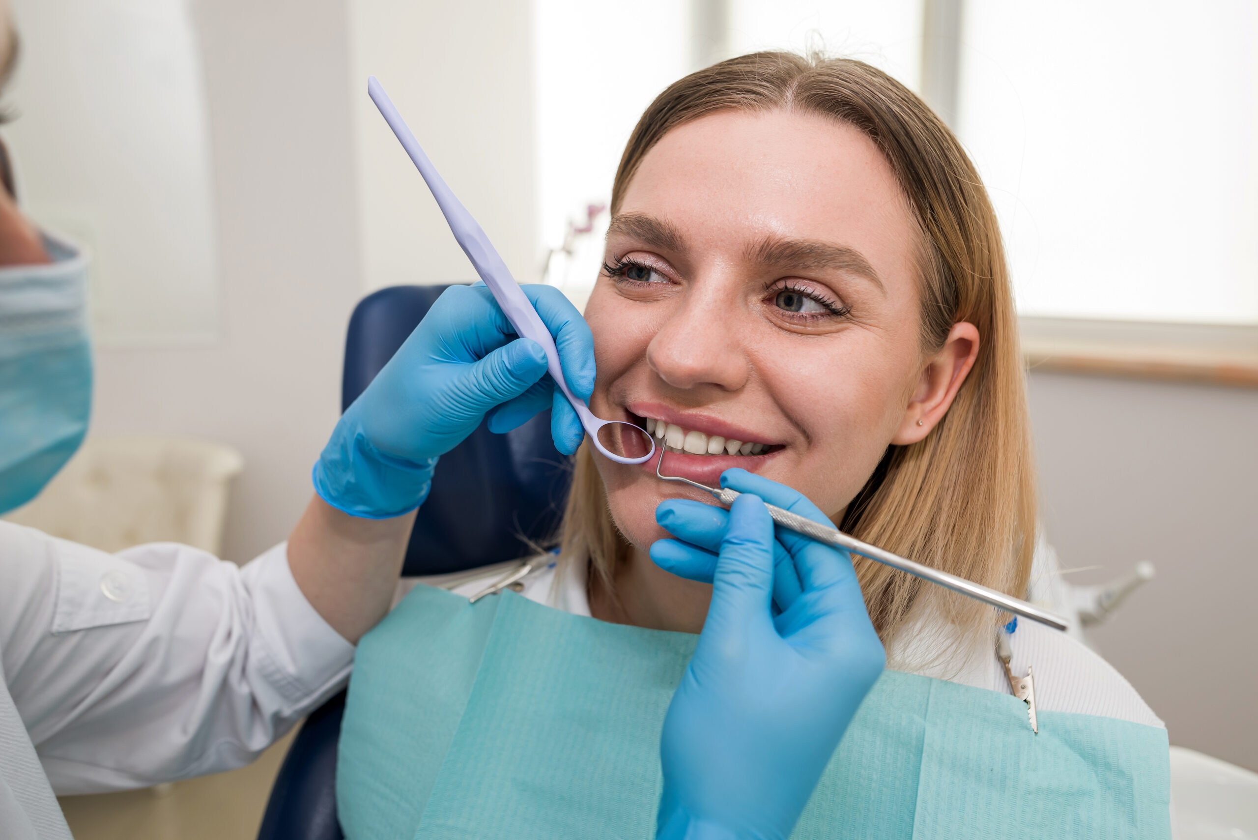 Close-up of a dentist in a mask and a patient, a dentist treating a cheerful young blonde patient smiling. Dentistry, modern dental clinic concept.