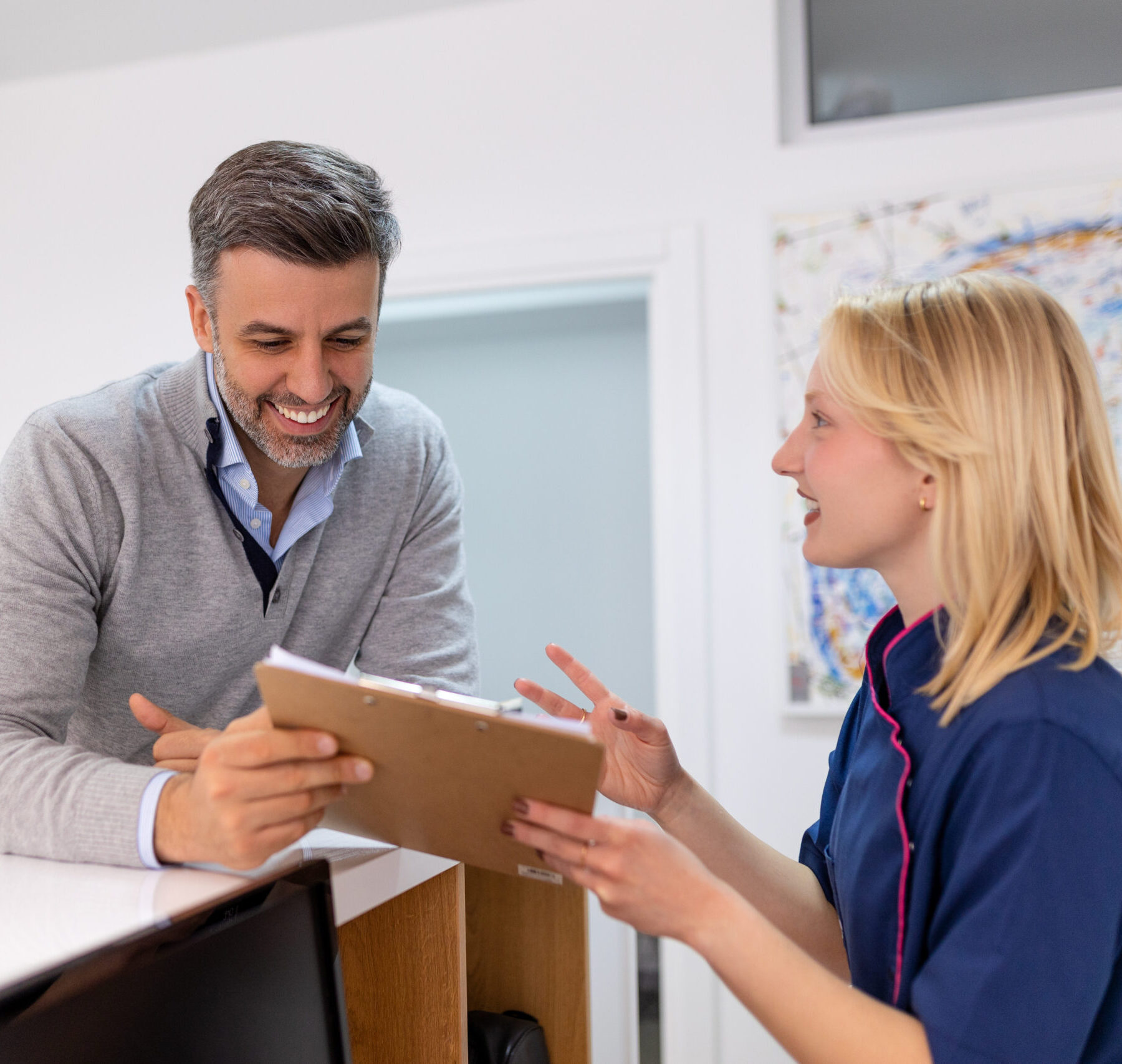 Supporting patients. Smiling man and his cheerful dentist together filling up a form at the reception desk.