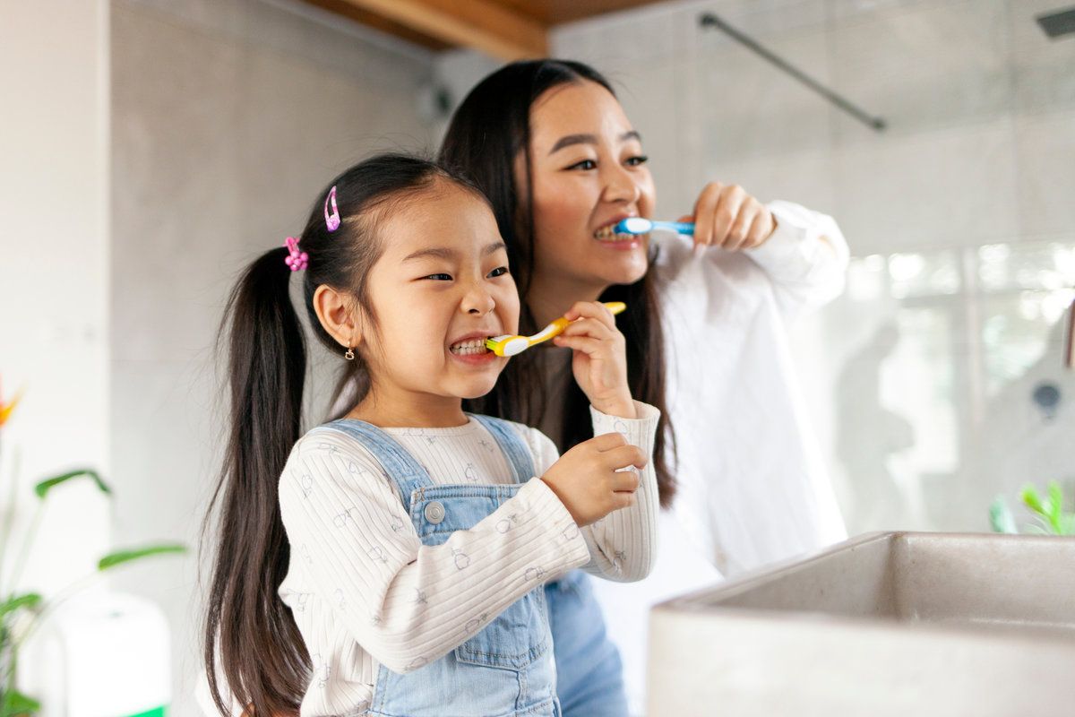 asian little girl with mom brushing teeth in bathroom, korean woman helping to brush daughter's teeth at home together